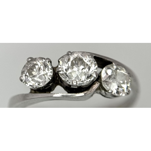 75 - An 18K White Gold Three Stone Diamond Crossover Ring. One central brilliant round cut diamond of 0.7... 