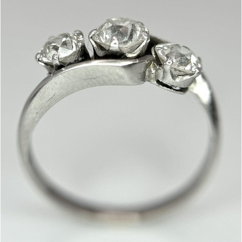 75 - An 18K White Gold Three Stone Diamond Crossover Ring. One central brilliant round cut diamond of 0.7... 