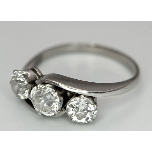 75 - An 18K White Gold Three Stone Diamond Crossover Ring. One central brilliant round cut diamond of 0.7... 