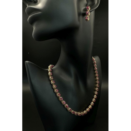 1415 - A Ruby and Diamond Tennis Necklace and Drop Earrings Set. Oval cut deep red rubies each with an old ... 