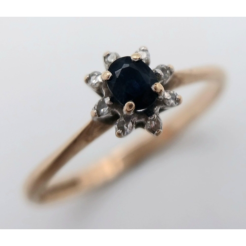 577 - A Petit 9K Yellow Gold Sapphire and Diamond Ring. A central sapphire with an eight diamond surround.... 