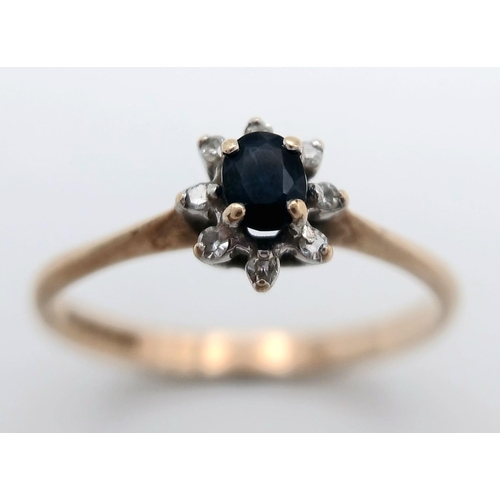 577 - A Petit 9K Yellow Gold Sapphire and Diamond Ring. A central sapphire with an eight diamond surround.... 