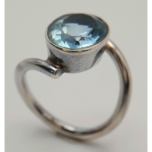 906 - A Sterling Silver Blue Topaz Set Crossover Ring Size N. Set with a 1.4cm Long Oval Cut Blue Topaz, t... 