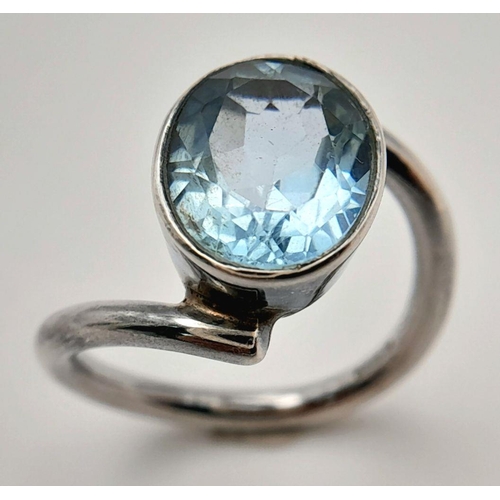 906 - A Sterling Silver Blue Topaz Set Crossover Ring Size N. Set with a 1.4cm Long Oval Cut Blue Topaz, t... 