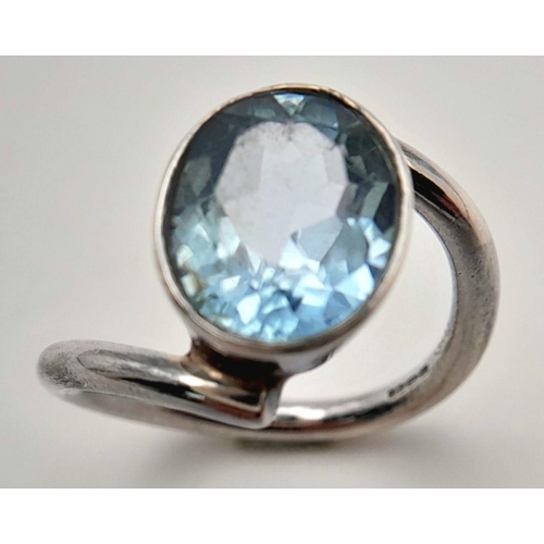 906 - A Sterling Silver Blue Topaz Set Crossover Ring Size N. Set with a 1.4cm Long Oval Cut Blue Topaz, t... 