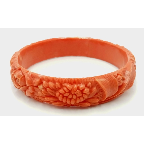 324 - A Vintage Bakelite Coral Coloured Bangle. Decorative floral carving. 63mm inner diameter.