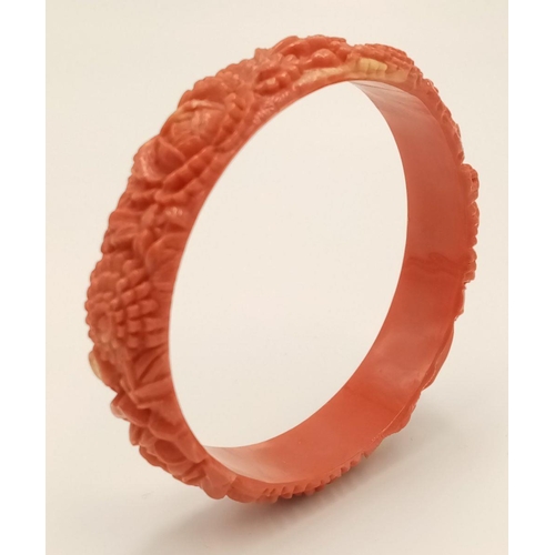 324 - A Vintage Bakelite Coral Coloured Bangle. Decorative floral carving. 63mm inner diameter.