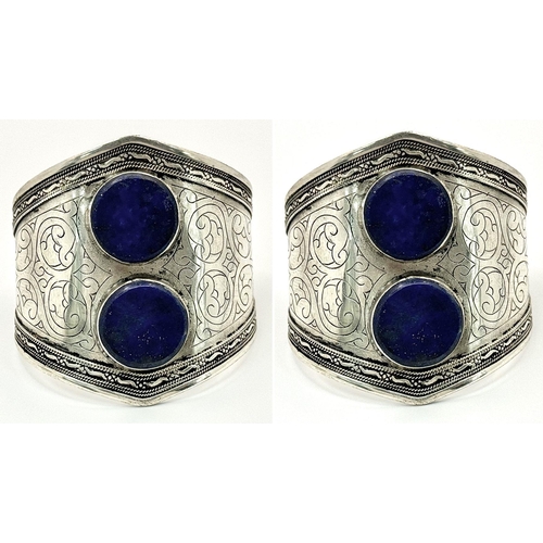 1524 - A Pair of Metal Cuff Bangles with Lapis Lazuli Centre Stones. Total weight: 107g