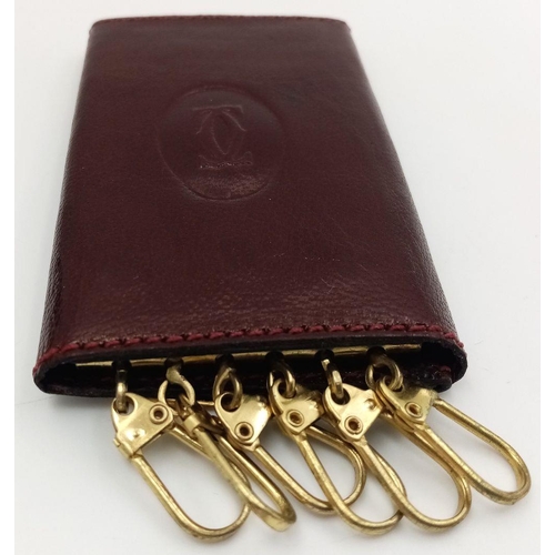 402 - A Cartier Burgundy Leather Key Holder. Leather exterior with gold-tone hardware and snap closure. Bu... 