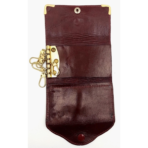 402 - A Cartier Burgundy Leather Key Holder. Leather exterior with gold-tone hardware and snap closure. Bu... 