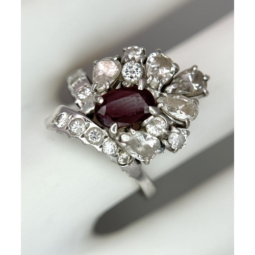 59 - A Vintage 18K White Gold, Ruby and Diamond Ring. An oval ruby with an abstract diamond surround of p... 