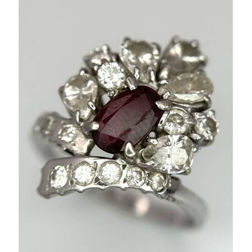 59 - A Vintage 18K White Gold, Ruby and Diamond Ring. An oval ruby with an abstract diamond surround of p... 