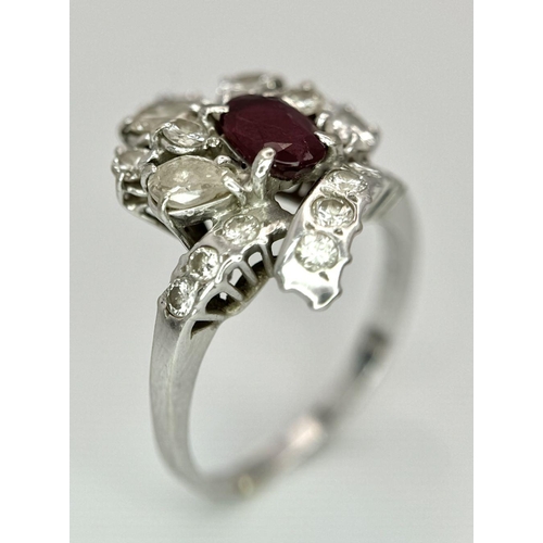 59 - A Vintage 18K White Gold, Ruby and Diamond Ring. An oval ruby with an abstract diamond surround of p... 