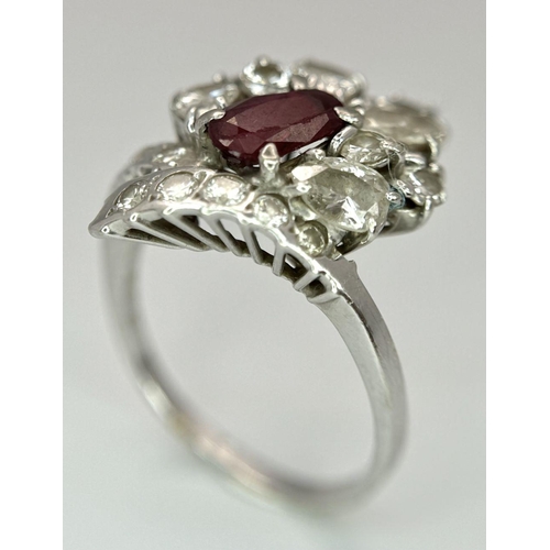 59 - A Vintage 18K White Gold, Ruby and Diamond Ring. An oval ruby with an abstract diamond surround of p... 