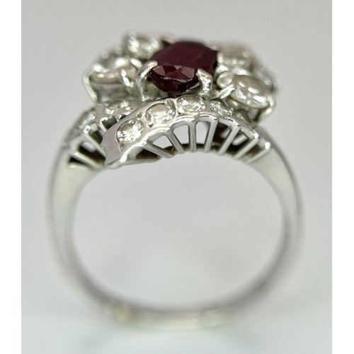 59 - A Vintage 18K White Gold, Ruby and Diamond Ring. An oval ruby with an abstract diamond surround of p... 