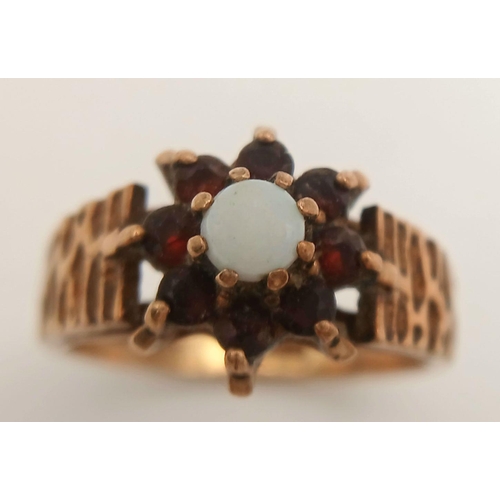 381 - A VINTAGE 9K GOLD RING WITH CENTRAL OPAL SURROUNDED BY GARNETS .     2.5gms    size K