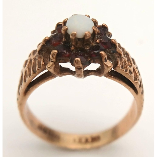 381 - A VINTAGE 9K GOLD RING WITH CENTRAL OPAL SURROUNDED BY GARNETS .     2.5gms    size K