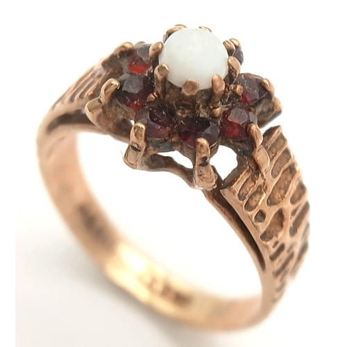 381 - A VINTAGE 9K GOLD RING WITH CENTRAL OPAL SURROUNDED BY GARNETS .     2.5gms    size K