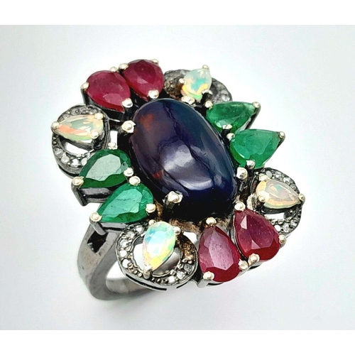 534 - A 925 silver ring featuring a central black opal, accented with emeralds, rubies, and moonstones, co... 