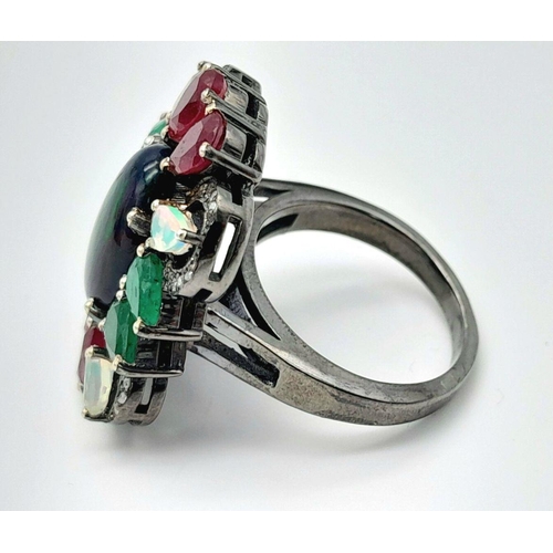 534 - A 925 silver ring featuring a central black opal, accented with emeralds, rubies, and moonstones, co... 