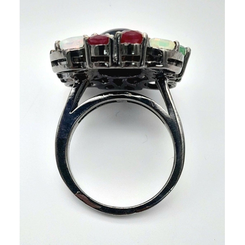 534 - A 925 silver ring featuring a central black opal, accented with emeralds, rubies, and moonstones, co... 