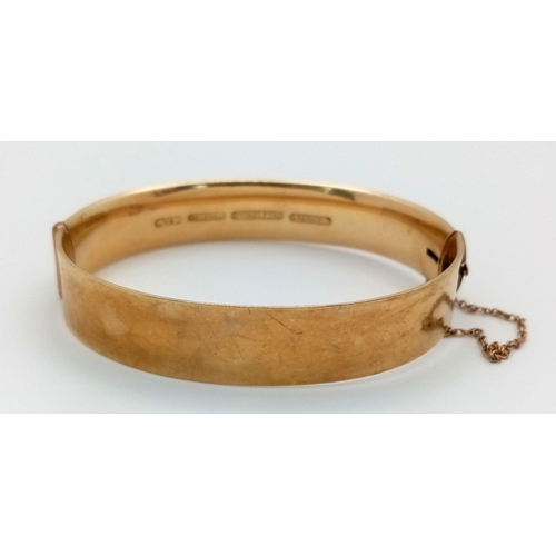 199 - A DECORATIVE HINGED BANGLE IN 9K GOLD WITH A BRONZE CORE COMES WITH SAFETY CHAIN AND IN VERY GOOD CO... 