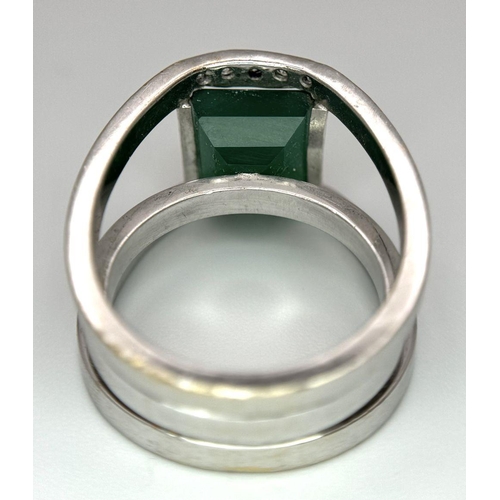 18 - A 21k White Gold, Emerald and Diamond Orbital Ring. A large 3ct square cut central emerald with diam... 