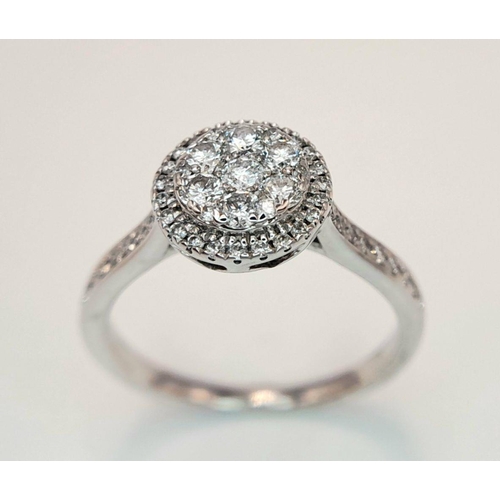 528 - A 9K White Gold Diamond Cluster Ring. Two circular levels and shoulders of diamonds. Size L 1/2. 3.4... 