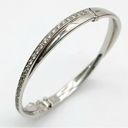 134 - A 9K White Gold White Stone Crossover Bangle. Clip design. 6cm inner diameter. 13.2g.