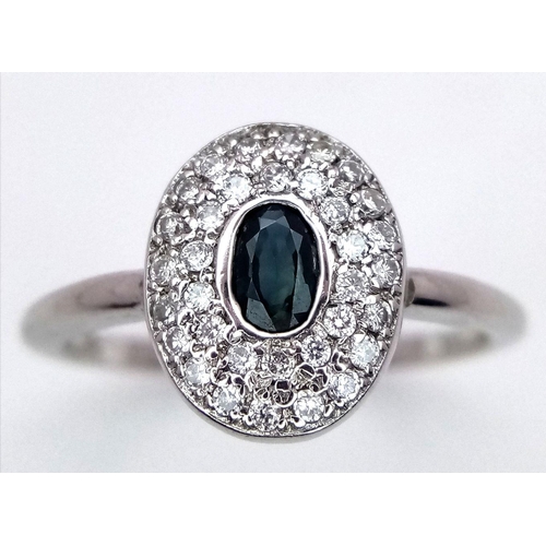 141 - An 18K White Gold Emerald and Diamond Ring. Central oval cut emerald with a diamond cluster surround... 