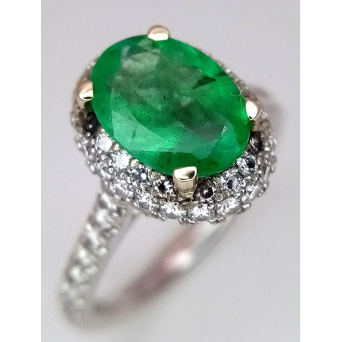 694 - A 14K White Gold, Emerald and Diamond Ring. A 1.3ct oval cut emerald with diamond surround and shoul... 