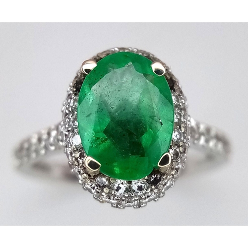 694 - A 14K White Gold, Emerald and Diamond Ring. A 1.3ct oval cut emerald with diamond surround and shoul... 