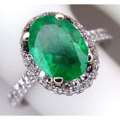 694 - A 14K White Gold, Emerald and Diamond Ring. A 1.3ct oval cut emerald with diamond surround and shoul... 