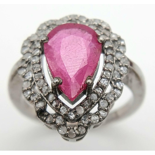 221 - A 925 silver ring featuring a 3.5ct pear-cut ruby, framed by two rows of intricate diamond accents. ... 