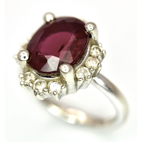 384 - A 14K White Gold, Garnet and Diamond Ring. Rich, oval cut central garnet with a twelve stone diamond... 