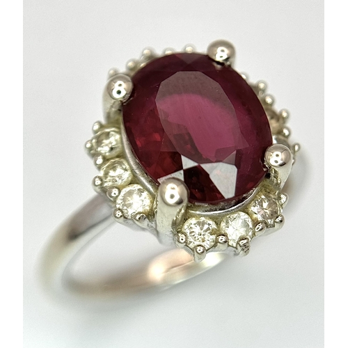 384 - A 14K White Gold, Garnet and Diamond Ring. Rich, oval cut central garnet with a twelve stone diamond... 