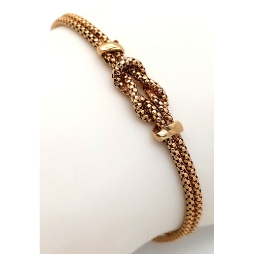 100 - A 9K Yellow Gold Serpentine Link Bracelet with Central Love Knot. 18cm. 4g