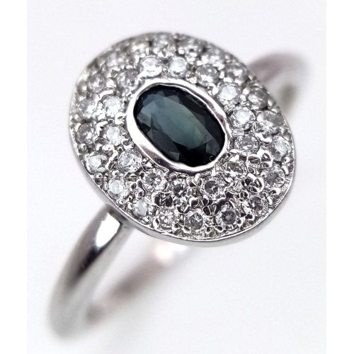 364 - An 18K White Gold Emerald and Diamond Ring. Central oval cut emerald with a diamond cluster surround... 