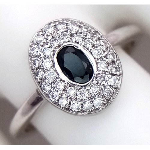 364 - An 18K White Gold Emerald and Diamond Ring. Central oval cut emerald with a diamond cluster surround... 