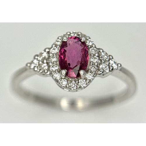 177 - An 18K White Gold, Ruby and Diamond Ring. 0.25ct oval cut high grade central ruby with a diamond clu... 