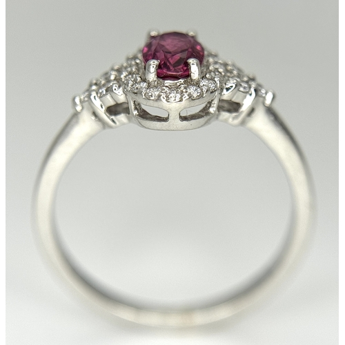 177 - An 18K White Gold, Ruby and Diamond Ring. 0.25ct oval cut high grade central ruby with a diamond clu... 
