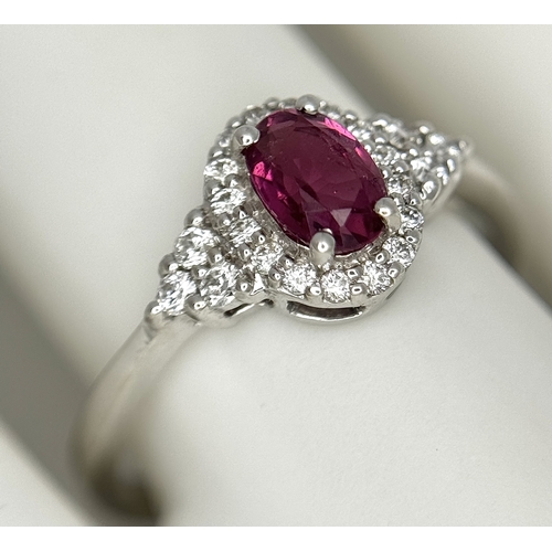 177 - An 18K White Gold, Ruby and Diamond Ring. 0.25ct oval cut high grade central ruby with a diamond clu... 