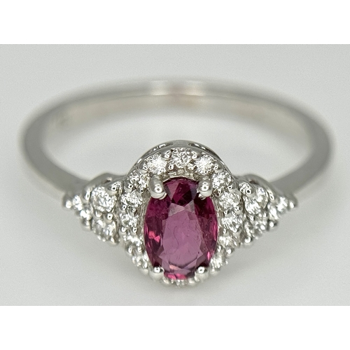 177 - An 18K White Gold, Ruby and Diamond Ring. 0.25ct oval cut high grade central ruby with a diamond clu... 