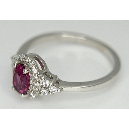 177 - An 18K White Gold, Ruby and Diamond Ring. 0.25ct oval cut high grade central ruby with a diamond clu... 