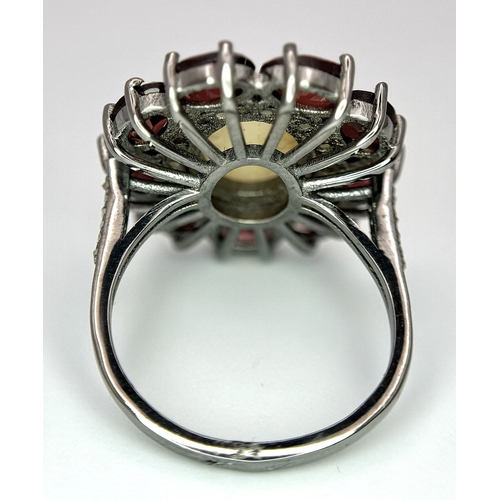 831 - An Opal, Garnet and Diamond Ring. Central 2ct opal cabochon with garnet and diamond surround. Set in... 