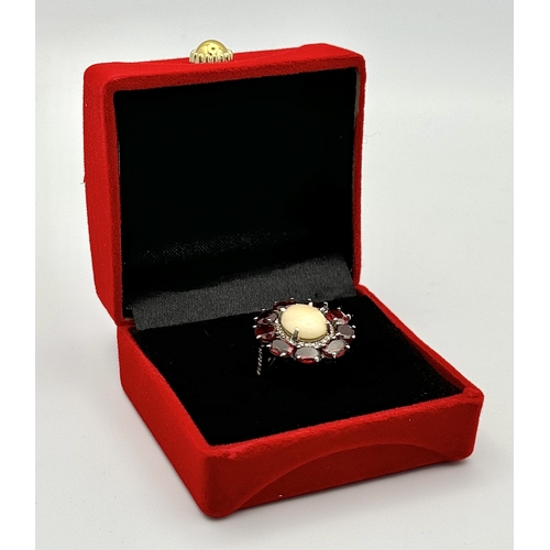 831 - An Opal, Garnet and Diamond Ring. Central 2ct opal cabochon with garnet and diamond surround. Set in... 