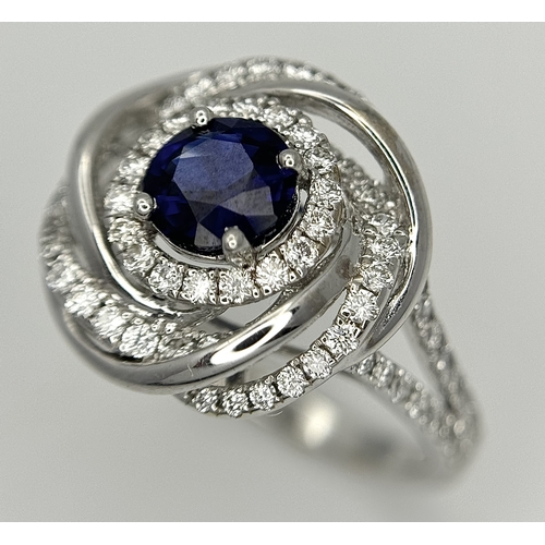 72 - An 18K White Gold, Diamond and Sapphire Swirl Ring. A 0.75ct round cut sapphire is the eye in a diam... 