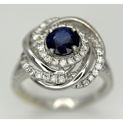 72 - An 18K White Gold, Diamond and Sapphire Swirl Ring. A 0.75ct round cut sapphire is the eye in a diam... 