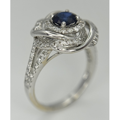 72 - An 18K White Gold, Diamond and Sapphire Swirl Ring. A 0.75ct round cut sapphire is the eye in a diam... 