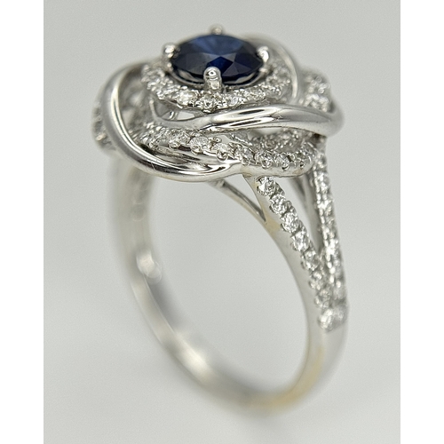 72 - An 18K White Gold, Diamond and Sapphire Swirl Ring. A 0.75ct round cut sapphire is the eye in a diam... 